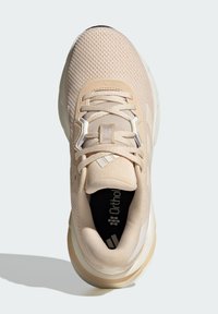 Chaussure de sport beige avec un matériau en maille respirant, un dessus texturé, un talon renforcé et des accents réfléchissants. Semelle intérieure Ortholite visible.