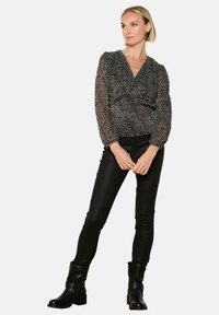 Blusa nera trasparente con design a stampa leopardata, dotata di scollo a V, maniche a sbuffo e vita arricciata. Abbinata a pantaloni neri attillati e stivali.