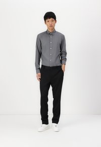 Grå knapp-up skjorta med krage, svarta byxor och vita sneakers. Slät tyg, åtsittande design och minimalistisk stil.