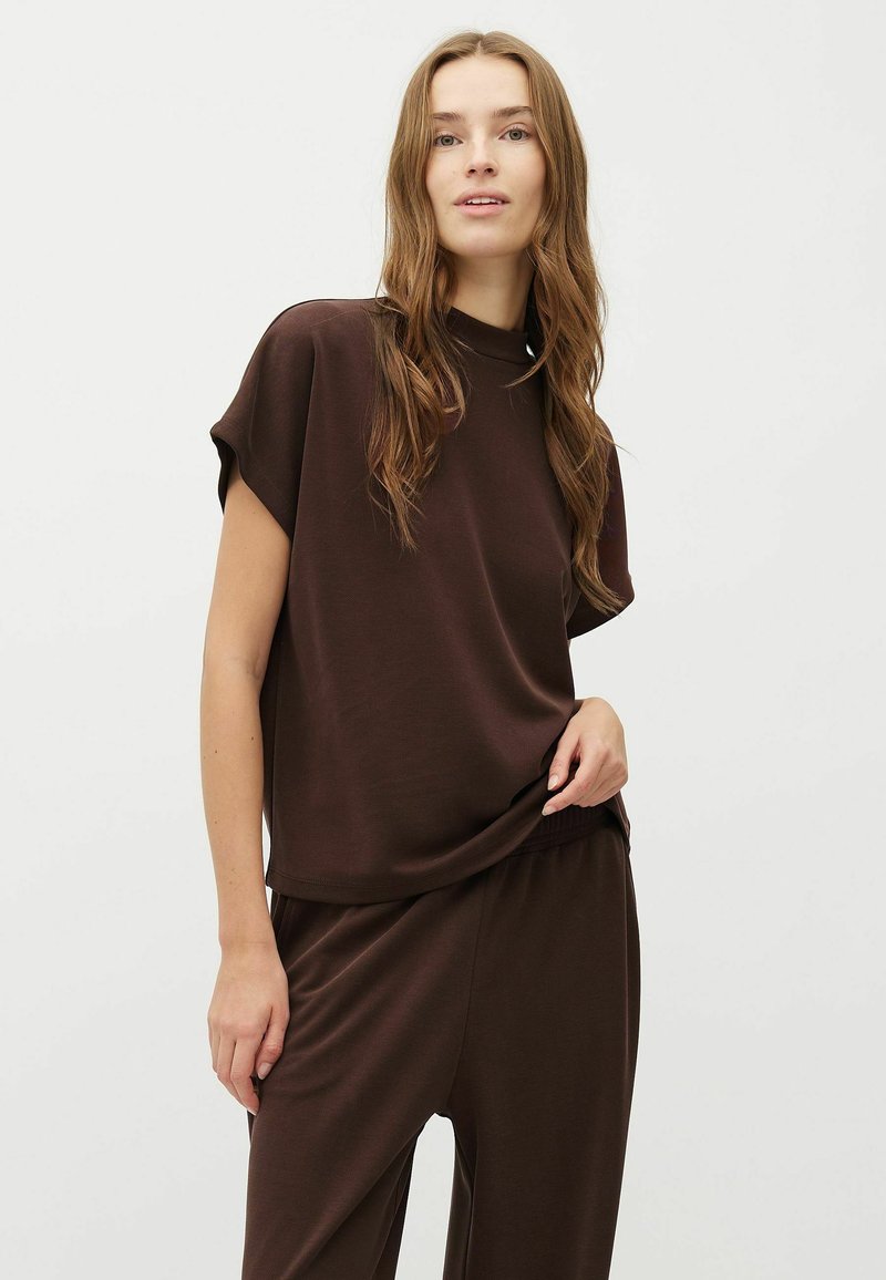 Bruine top met korte mouwen en een hoge halslijn, gecombineerd met bijpassende loszittende broek. Gladde textuur en ontspannen silhouet.