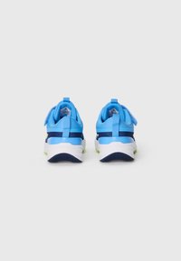 Des chaussures de sport bleues avec une tige lisse, des accents bleu marine contrastants, une semelle intermédiaire blanche et une semelle en caoutchouc texturée. Elles possèdent un tirant au niveau du talon.