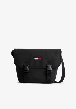 Sort Tommy Jeans crossbody-taske med klap, to spænder og justerbar skulderrem på hvid baggrund.