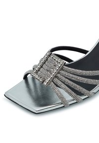Décolleté argentato a punta quadrata con cinturino decorato con cristalli, dotato di una grande fibbia rettangolare e superficie lucida e riflettente.