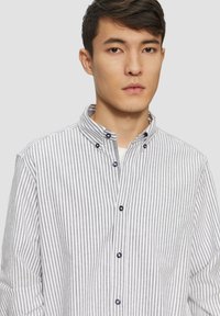 Camisa de botones a rayas en blanco y gris, con un cuello extendido y botones en contraste en color marino, con mangas largas y una tela texturizada.