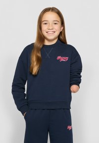 Sudadera azul marino con puños y dobladillo acanalados, con un logo rojo de "Tommy" en el pecho. Tejido suave, corte relajado. Combinada con pantalones a juego.