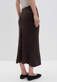 Gonna marrone di media lunghezza con una texture liscia e design svasato. Indossata con ballerine nere. Stile minimalista su uno sfondo neutro.