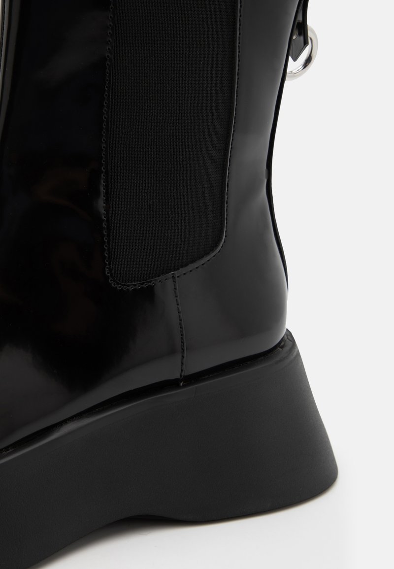 Czarne lakierowane botki za kostkę z teksturowanym czarnym elastycznym panelem po bokach oraz grubą, matową czarną gumową podeszwą. Akcenty w kolorze srebrnym.
