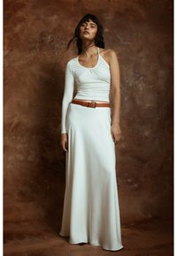 Haut blanc à col halter avec une manche longue, associé à une jupe blanche fluide et une ceinture en cuir marron. Texture lisse et lignes épurées.