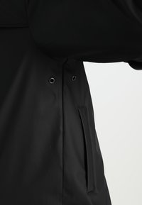 Svart vattentät jacka med en slät yta, tryckknappar och sidofickor, med en elegant design och minimalt med detaljer.