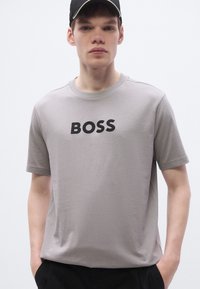 Γκρι βαμβακερό t-shirt με κοντά μανίκια, με μαύρο λογότυπο "BOSS" στο κέντρο του στήθους. Λεία υφή, στρογγυλή λαιμόκοψη.