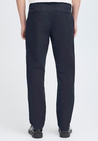 Chinos bleu marine foncé en tissu mélangé coton, dotés de deux poches arrière avec fermetures à bouton et d'une coupe droite. Texture lisse et ajustement sur mesure.