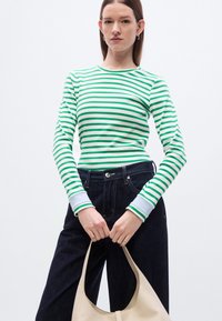 Πράσινο και λευκό ριγέ μακρυμάνικο τοπ με στρογγυλή λαιμόκοψη· συνδυασμένο με σκούρο μπλε τζιν και κρατώντας μια μπεζ τσάντα tote.