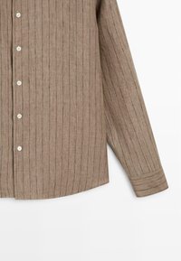 Chemise marron à manches longues avec des rayures noires verticales, des boutons blancs sur le devant et des poignets boutonnés, sur fond blanc.
