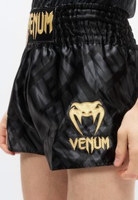 Μαύρα σατινέ σορτς με ελαστική μέση, με χρυσό λογότυπο "VENUM" και σχέδιο αράχνης, με διακριτικό τονικό σχέδιο σε όλο το ύφασμα.