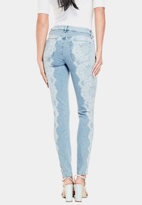 Jeans skinny de color azul claro con un patrón de encaje a lo largo de las costuras exteriores, con un diseño de cintura alta y bolsillos traseros. Los zapatos son metálicos.