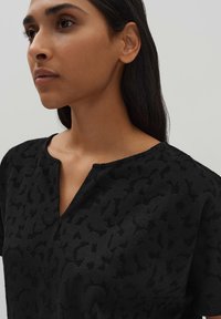 Zwarte top met een gestructureerd patroon, korte mouwen en een V-halsontwerp. De stof lijkt zacht en licht textuurd te zijn.