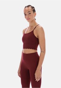 Bordowy stanik sportowy z falbaniastym wykończeniem, regulowanymi ramiączkami i dopasowanym krojem. Noszony z pasującymi legginsami o wysokim stanie.