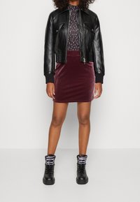 Chaqueta de cuero negra corta con dos bolsillos en el pecho, una blusa estampada, una falda mini de terciopelo burdeos y unas botas negras con cordones grises.