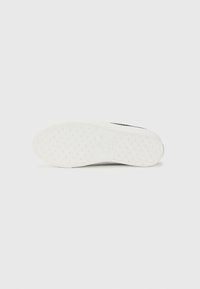 White sneaker sole with textured rubber for grip, featuring a simple design and embossed logo detail. Clean, minimalistic aesthetic.