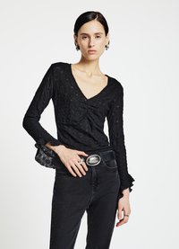 Haut noir texturé à manches longues avec un col en V et des poignets à volants, associé à un jean noir taille haute et une large ceinture avec une boucle argentée.