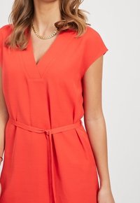 Czerwona sukienka z dekoltem w kształcie litery V i krótkimi rękawami w formie bufek. Posiada pasek w talii oraz teksturowany materiał dla miękkiego wykończenia.