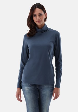 Dunkelblaues langärmeliges Rollkragenoberteil aus glattem, elastischem Stoff, kombiniert mit hellblauen, lädierten Jeans. Schlichtes, figurbetontes Design.