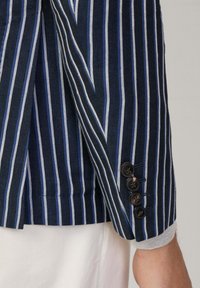 Marinblå randig blazer med tunna blå och vita ränder, med en strukturerad tygkvalitet, knäppta manschetter och en grå tygdetalj på ärmarna.