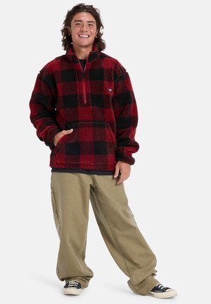 Rood en zwart geruite fleece pullover met een kwart rits. Gecombineerd met losse beige broeken en zwarte sneakers, wat een relaxte pasvorm laat zien.