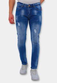 Lichtblauwe denim jeans met een slim fit, voorzien van versleten details en een vervaagde wassing. Gecombineerd met witte sneakers voor contrast.