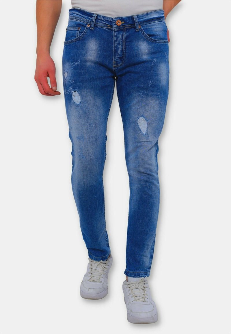Lichtblauwe denim jeans met een slim fit, voorzien van versleten details en een vervaagde wassing. Gecombineerd met witte sneakers voor contrast.