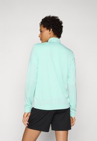 Light blue zip-up jacket made of smooth material, featuring a collared neck and ribbed cuffs, paired with black shorts.