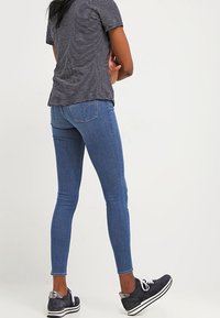 Jeans de denim azul ajustados con bolsillos traseros, combinados con una camiseta de rayas en blanco y negro y zapatillas oscuras.