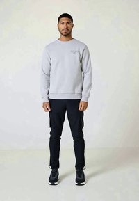 Gray sweatshirt with ribbed cuffs, crew neckline, and front logo; paired with black cargo pants and black athletic shoes. Simple design.