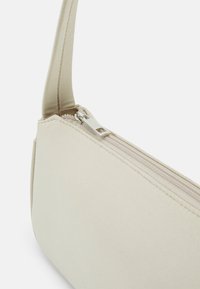 Borsa beige con una texture liscia, dotata di una lunga tracolla e di una chiusura con zip lungo la parte superiore. Design minimalista con linee pulite.