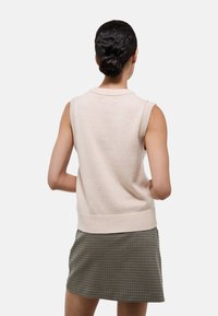 Pull sans manches rose clair avec des bordures côtelées et un col rond, associé à une mini jupe à carreaux noir et blanc. Texture lisse.