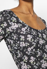 Haut à motifs floraux avec une base noire, présentant de petites fleurs roses et vertes. Encolure arrondie et design ajusté. Texture de tissu extensible.