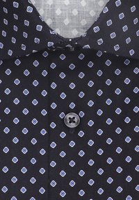 Chemise noire avec un motif géométrique bleu et blanc, dotée d'un bouton et d'un col structuré. Tissu texturé avec une finition lisse.
