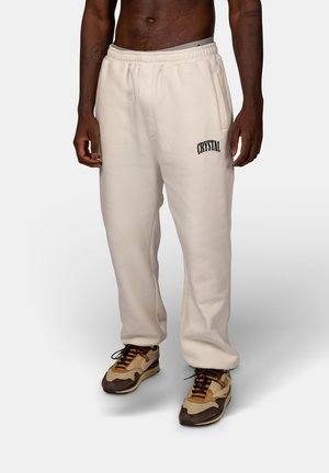 Cream-colored sweatpants with an elastic waistband and side pockets, featuring "CRYSTAL" embroidered in black on the left thigh.