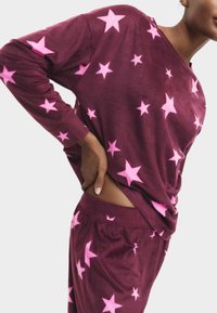 Conjunto de loungewear burdeos con mangas largas y patrones de estrellas rosas. Tejido suave con un corte relajado. Cintura visible y detalle lateral.