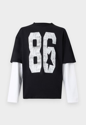 T-shirt preta oversized com mangas compridas brancas, apresenta uma grande estampa branca "86" e um gráfico de estrela nas costas. Material de algodão.