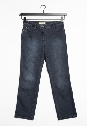 Jean en denim bleu foncé avec une coupe droite, cinq poches, un délavage subtil et une taille avec passants de ceinture. Suspendu à un cintre en métal noir.