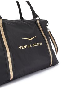 Black nylon duffel bag with gold accents and logo "VENICE BEACH," featuring two striped handles and adjustable shoulder strap.