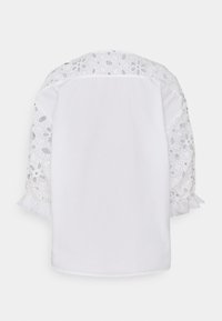 Blusa bianca con dettagli in pizzo sulle spalle e sulle maniche, maniche gonfie con volant e un design posteriore semplice e pulito.
