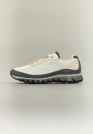 Chaussure de sport blanche et grise à profil bas avec semelle texturée et tige en mesh, vue de côté sur fond uni.