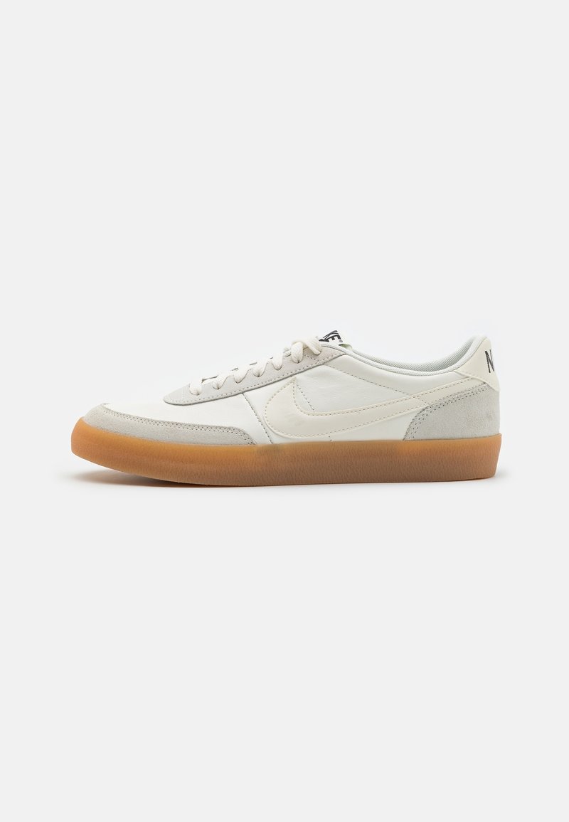 Baskets blanches basses avec des accents en daim beige, semelle en caoutchouc gomme et lacets blancs, vues de côté sur un fond uni.