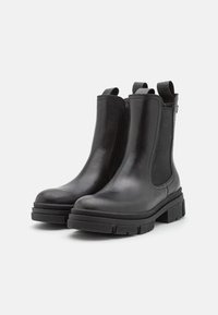 Černé kožené Chelsea boty s elastickými bočními panely, zaoblenými špičkami a silnými gumovými podrážkami s texturovaným vzorem.