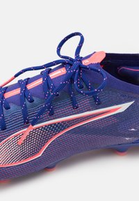 Blauw en roze voetbalschoen met een gestructureerde bovenkant, meerdere veters, een reflecterende zilveren accenten en ronde noppen op de zool.