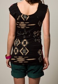 Top senza maniche nero con motivi geometrici beige, design delle spalle arricciato, abbinato a pantaloni shorts verdi. Tessuto liscio e stile aderente.