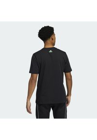 T-shirt noir à manches courtes en coton, avec un col rond et un logo Adidas vert au dos. Texture lisse et coupe décontractée.