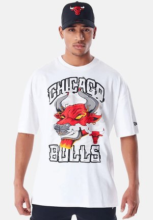 Weißes T-Shirt mit kurzen Ärmeln, das ein großes rotes Bullensymbol, schwarzen Text "CHICAGO BULLS" und einen lockeren Schnitt zeigt. Schwarze Mütze mit Bullensymbol.
